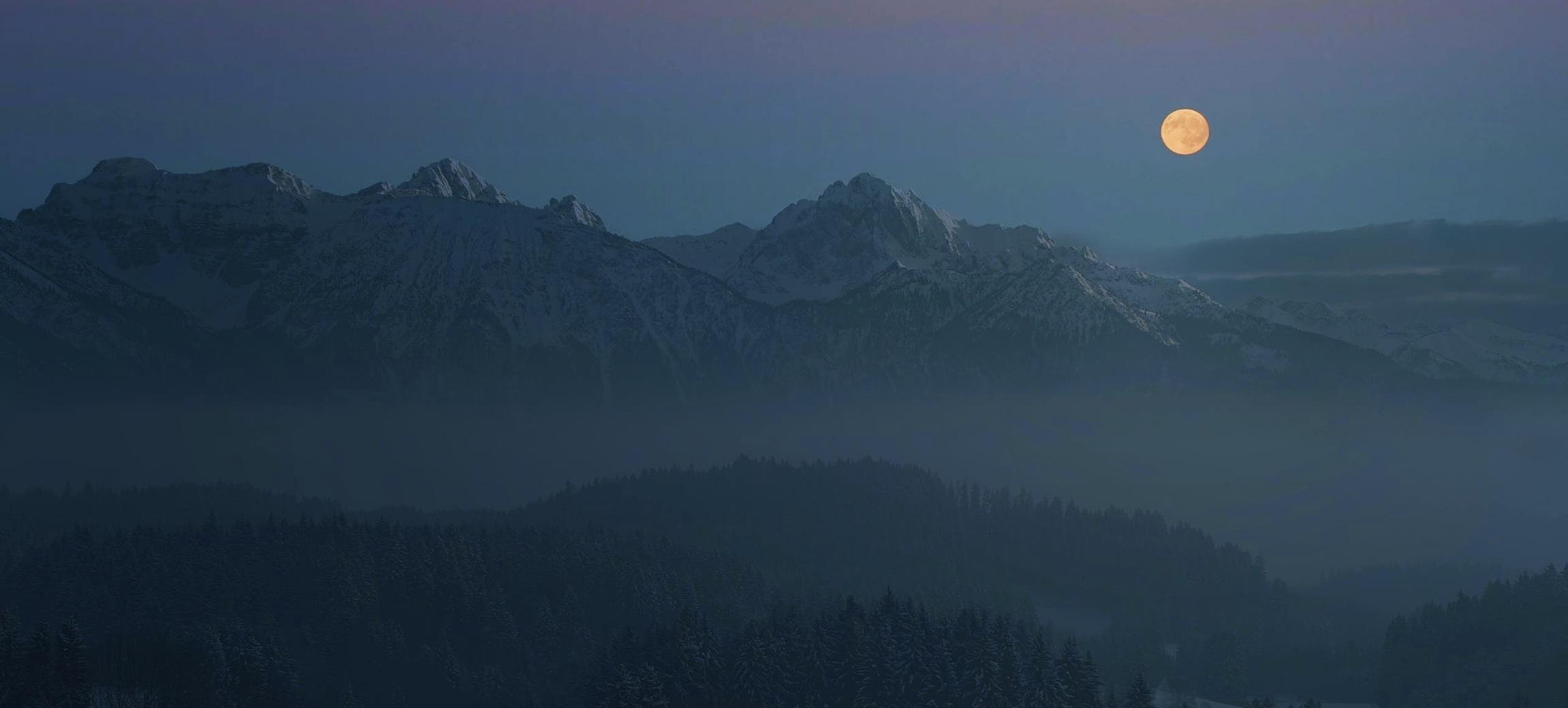 Full moon rising over a hazy mountain landscape at dusk
