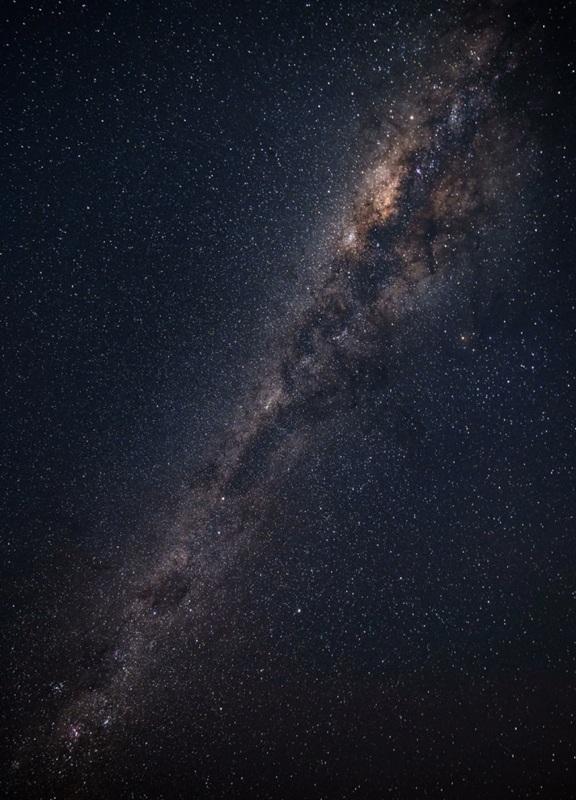 Star-filled night sky showing the Milky Way above dark terrain